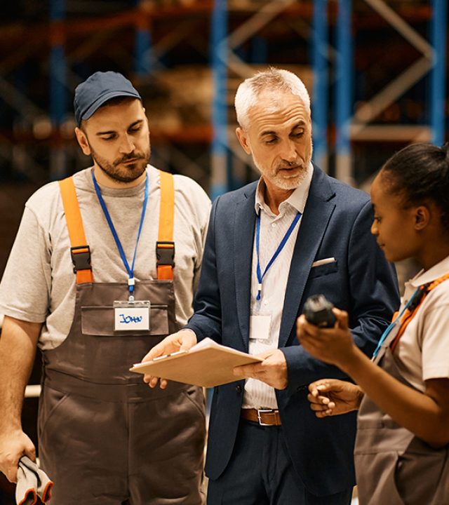 Young workers communicating with senior inspector at distribution warehouse.